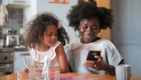 Child Tax Credit income level Increase for 2024 Black Woman with girl child sit at kitchen table looking at smart phone (Photo - Pexels-Andrea Piacquadio)